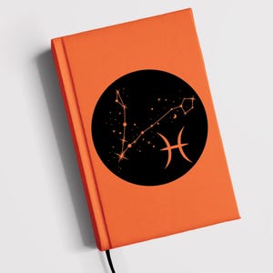May include: Orange notebook with a black circle containing a constellation of stars and the Pisces zodiac symbol.