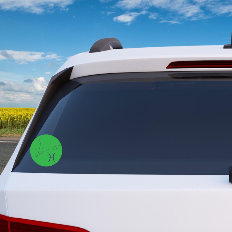 May include: A white car with a green circle sticker on the back window. The sticker features a black outline of the Pisces constellation with the Pisces symbol.