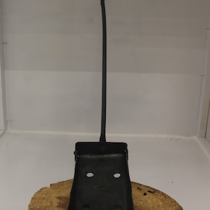 May include: Black metal fireplace poker with a twisted handle and a scoop at the end. The poker is resting on a wooden surface.