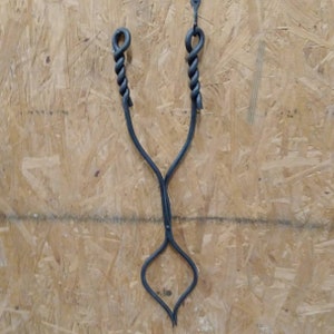 May include: Black metal fireplace tongs with twisted handles. The tongs are designed to grab and lift logs in a fireplace.