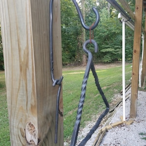 May include: A black metal triangle chime hanging from a hook attached to a wooden post. The chime is twisted and has a rustic look.