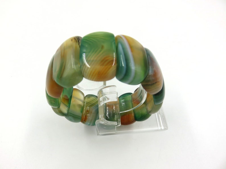 May include: A green, brown, and white agate stone bracelet with a polished finish. The bracelet is made of multiple round beads that are strung together.