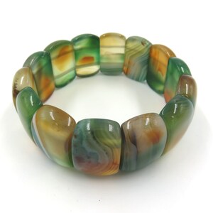 May include: A green, brown, and white agate stone bracelet with a polished finish. The bracelet is made of multiple oval-shaped beads.