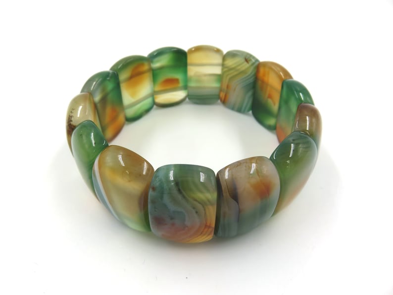 May include: A green, brown, and white agate stone bracelet with a polished finish. The bracelet is made of multiple oval-shaped beads.