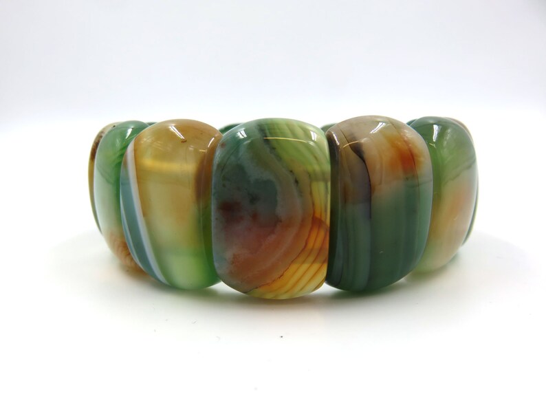 May include: A green, brown, and white agate stone bracelet with oval-shaped beads.