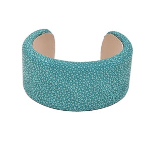 Puede incluir: Un brazalete de cuero azul turquesa con una superficie texturizada.