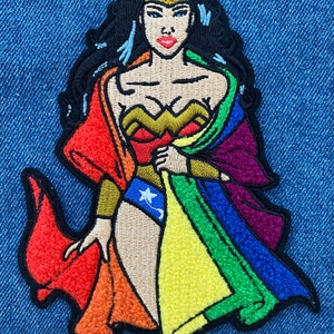 May include: Embroidered patch featuring Wonder Woman in a rainbow-colored cape. The cape is made up of the colors of the rainbow flag. Wonder Woman is wearing her traditional costume, including a red bodice, blue skirt, and a golden tiara with a red star.