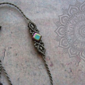 May include: A grey macrame bracelet with an iridescent square bead at its centre. The bracelet has an adjustable sliding knot closure. This handcrafted bracelet is a stylish accessory. The macrame design adds a touch of bohemian flair to the bracelet.