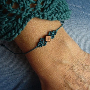 Puede incluir: Un brazalete de amistad azul turquesa con una cuenta de madera cuadrada en el centro.