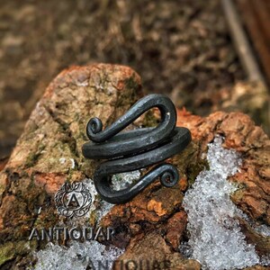May include: A black metal ring with a twisted design. The ring is made of forged steel and has a rustic look.