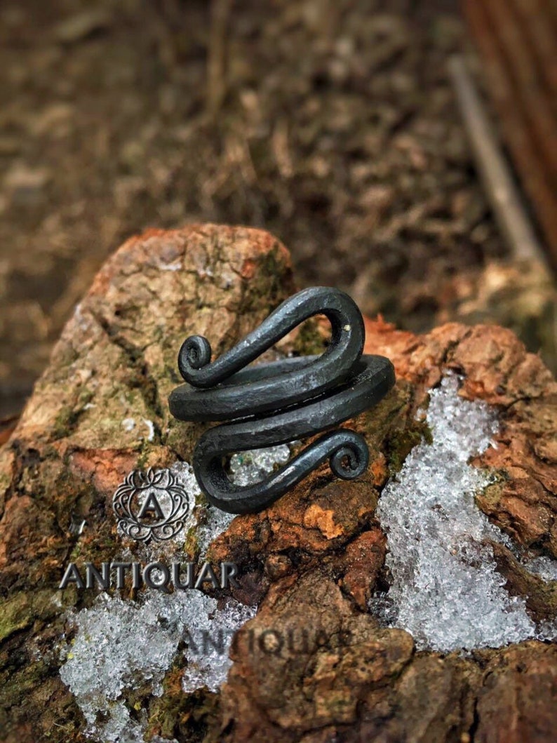 May include: A black metal ring with a twisted design. The ring is made of forged steel and has a rustic look.