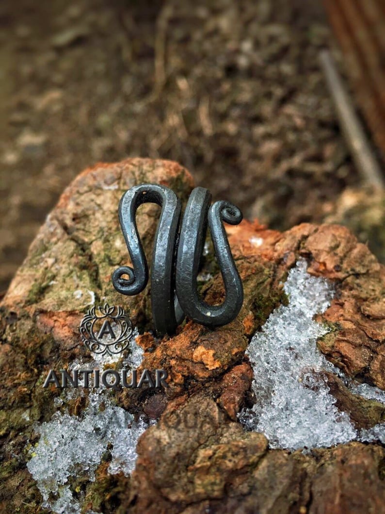 May include: A black metal ring with a unique, twisted design. The ring is handcrafted and has a rustic, antique look.