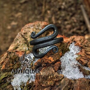 May include: A black metal ring with a unique, twisted design. The ring is handcrafted and has a rustic, antique look.