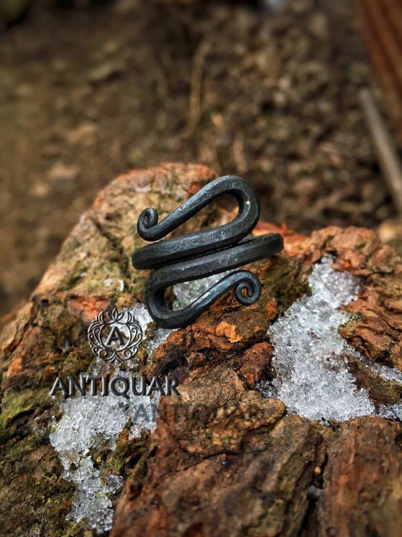 May include: A black metal ring with a unique, twisted design. The ring is handcrafted and has a rustic, antique look.