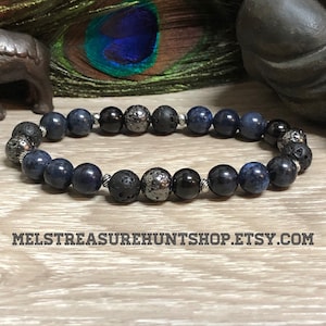 Pode incluir: Um bracelete de contas azuis e pretas com espaçadores prateados. O bracelete apresenta contas azuis escuras, pretas e cinzas.