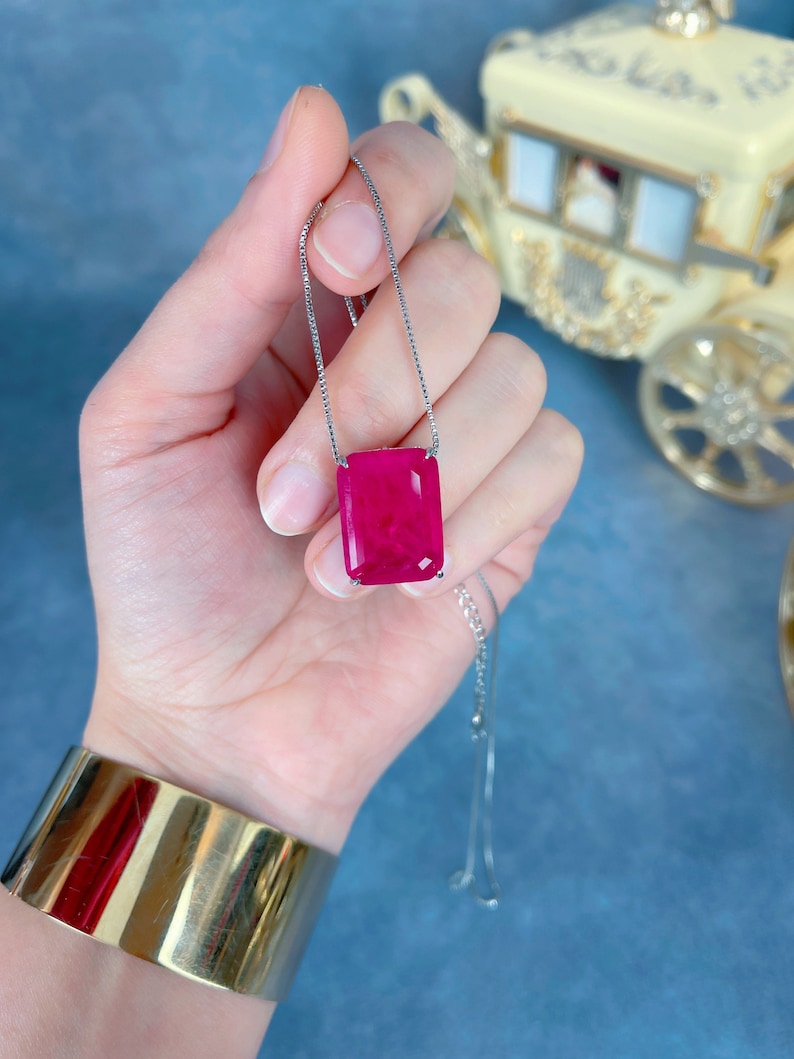 May include: A silver chain necklace with a large, rectangular, faceted, pink gemstone pendant.