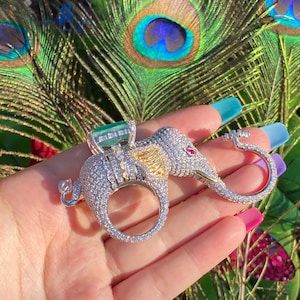 Peut inclure: Une bague en argent et or en forme d'éléphant avec une grande émeraude verte et de petites pierres rouges. La bague est sertie de diamants blancs scintillants.