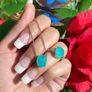 May include: A silver necklace and ring set featuring a turquoise gemstone. The necklace has a delicate chain and a round pendant with a turquoise stone. The ring has a similar turquoise stone and a silver band.