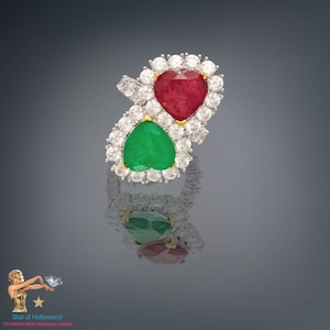 Puede incluir: Un anillo de oro con dos piedras preciosas en forma de corazón. El corazón superior es rojo y el corazón inferior es verde. Ambos corazones están rodeados de diamantes más pequeños.