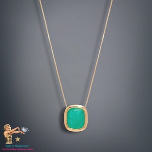 Könnte beinhalten: Eine goldene Kettenkette mit einem grünen Edelstein-Anhänger. Der Anhänger ist rechteckig mit abgerundeten Ecken und einem goldenen Rahmen.