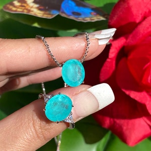 May include: A silver necklace and ring set featuring a large oval turquoise gemstone. The necklace has a delicate chain and the ring has three smaller gemstones on the side.