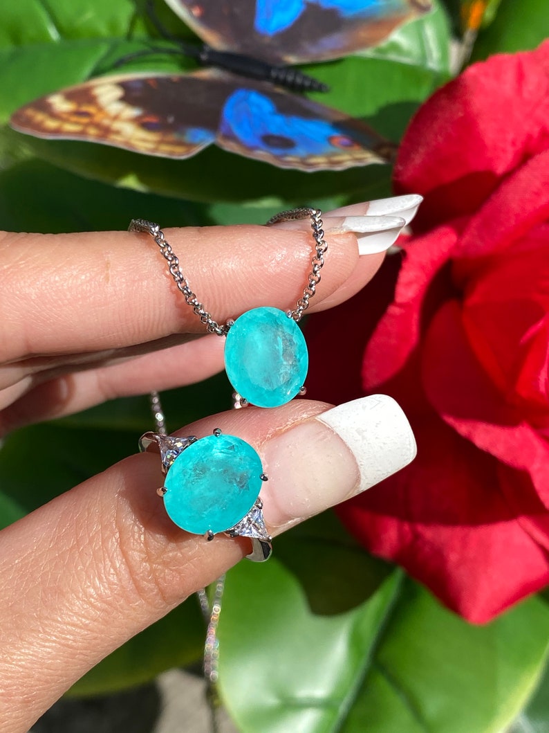 May include: A silver necklace and ring set featuring a large oval turquoise gemstone. The necklace has a delicate chain and the ring has three smaller gemstones on the side.