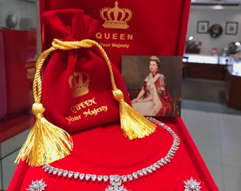 May include: A red velvet jewelry box with a gold crown and the words "Queen Your Majesty" on the lid. Inside the box is a silver necklace with a large, clear, square-shaped pendant and matching earrings. The necklace and earrings are set with small, clear stones.