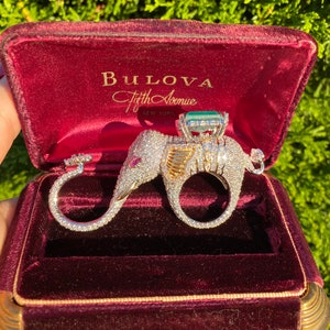 Peut inclure: Une bague Bulova Fifth Avenue représentant un éléphant serti de diamants tenant une grosse émeraude. La bague est présentée dans un écrin en velours rouge.