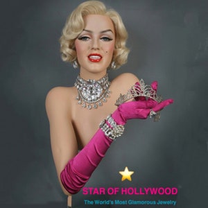May include: A mannequin with blonde hair wearing a diamond necklace, a tiara, and pink satin gloves. The mannequin is holding the tiara in her right hand. The text "STAR OF HOLLYWOOD" and "The World's Most Glamorous Jewelry" is below the mannequin.