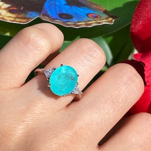 May include: A silver ring featuring a large oval turquoise gemstone, surrounded by smaller clear gemstones.