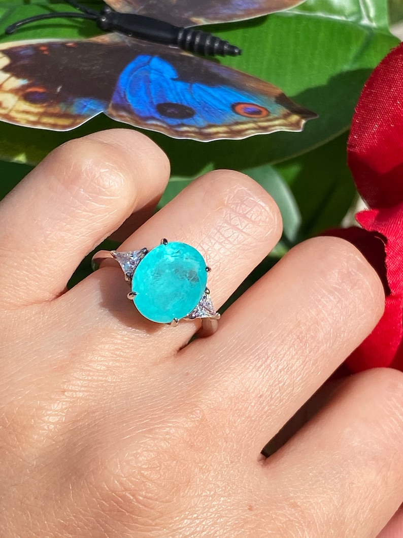 May include: A silver ring featuring a large oval turquoise gemstone, surrounded by smaller clear gemstones.