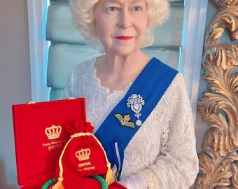 May include: A woman wearing a white lace dress, a blue sash, and a crown holds a red velvet box with a green jade necklace and a red velvet bag with gold embroidery that reads "Queen Your Majesty".