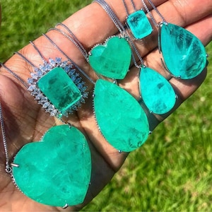 Puede incluir: Un conjunto de cinco collares de piedras preciosas de color verde esmeralda con cadenas de plata y diferentes formas de colgantes, incluyendo un corazón, una lágrima, un cuadrado y un colgante rectangular.
