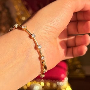 May include: A gold bracelet with multiple clear, round gemstones. The bracelet is made of gold-colored metal and is worn on a wrist. The gemstones are evenly spaced along the bracelet's length, reflecting light.