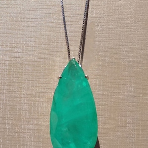 May include: A silver necklace featuring a large, pear-shaped, vibrant green gemstone pendant. The gemstone is faceted, catching the light, and is held in place by small silver prongs. The chain is delicate and hangs from the top of the pendant.