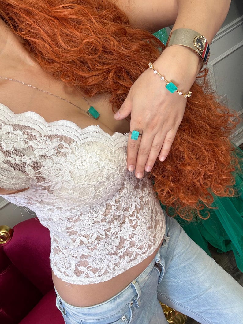 May include: A white lace top paired with light wash jeans. A silver necklace with a rectangular turquoise pendant, a matching ring, and a bracelet with turquoise accents are visible. A gold watch is also worn.