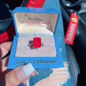 May include: A red gemstone ring in a blue ring box with the words "Star of Hollywood" and "The World's Most Glamorous Rings" on the lid.