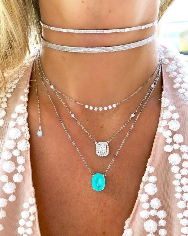May include: A layered silver necklace with a turquoise gemstone pendant and a smaller diamond pendant. The necklace features a delicate chain with small diamonds and a thicker chain with a square diamond pendant.