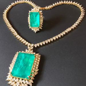 Op de afbeelding: Een gouden ketting- en ringset met grote smaragdgroene edelstenen omringd door kleinere heldere edelstenen.