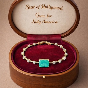 May include: A gold bracelet with a square, turquoise-colored center stone and clear accent stones, displayed in an open wooden jewelry box lined with red velvet. The box lid reads "Star of Hollywood Gems for Lady America."