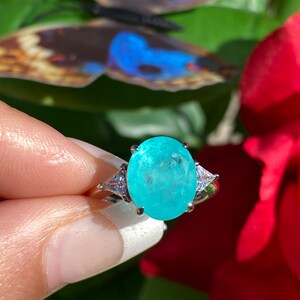 May include: A silver ring featuring a large oval turquoise gemstone, surrounded by smaller clear gemstones.