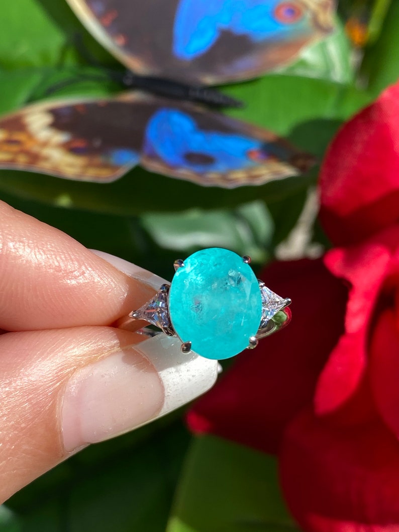 May include: A silver ring featuring a large oval turquoise gemstone, surrounded by smaller clear gemstones.