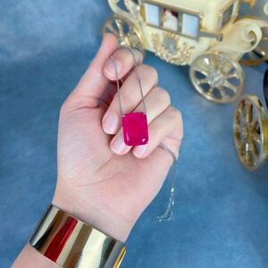 May include: A silver chain necklace with a large, rectangular, bright pink gemstone pendant.