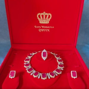 May include: A red velvet jewelry box with a gold crown and the text "Every Woman is a Queen". The box contains a ruby and diamond necklace, a pair of earrings, and a pendant.