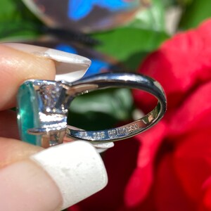 May include: A silver ring featuring a large, oval-shaped green gemstone and a smaller, round clear gemstone. The ring is marked "925 Princess" on the inside band.