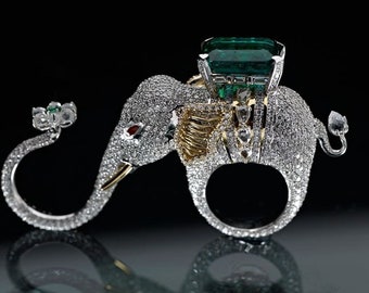 May include: A silver ring shaped like an elephant with a large green emerald gemstone on its back. The elephant is covered in small diamonds.