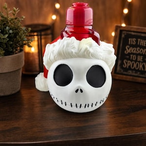 May include: A red plastic soap dispenser shaped like a skull with large black eye sockets and a stitched mouth. The skull is wearing a white Santa hat with a red top section. The pump mechanism is located at the top of the red Santa hat portion.