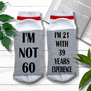May include: A pair of gray socks with red and white stripes at the top. One sock says "I'm not 60" and the other sock says "I'm 21 with 39 years experience".