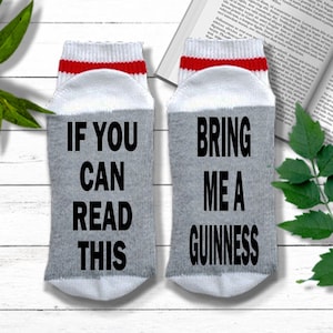 K&ouml;nnte beinhalten: Ein Paar graue und wei&szlig;e Socken mit rotem Besatz. Eine Socke sagt "Wenn du das lesen kannst" und die andere Socke sagt "Bring mir ein Guinness".
