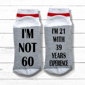 May include: A pair of gray and white socks with red stripes. One sock says "I'm not 60" and the other sock says "I'm 21 with 39 years experience".